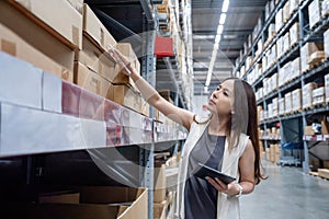Young smart asian business working woman using digital tablet to check goods on shelves for product management in warehouse,