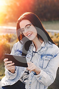 Young smart brunette woman in glasses using tablet outdoor