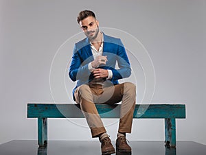 Seated smart casual man in blue suit fixes his cuffs