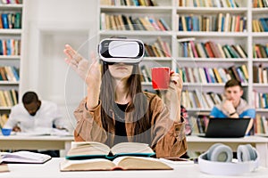 Young smart confident woman in casual clothes sitting in library and experiencing new device VR headset for study