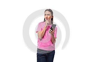 young smart good-looking woman with black hair dressed in a pink t-shirt holding a smartphone and looking away