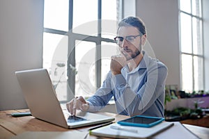 Young smart man with glasses looking at a laptop.