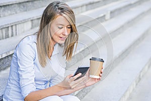 Young smart professional woman reading using phone. Female businesswoman reading news or texting sms on smartphone while drinking