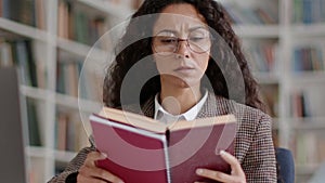 Young smart woman student reading book in college library, studying topic or making research, tracking shot