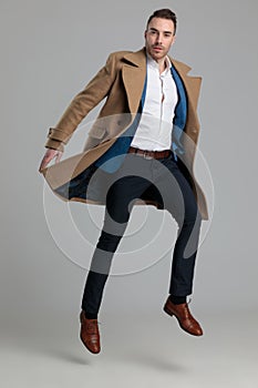 Young smartcasual guy in longcoat jumping in the air