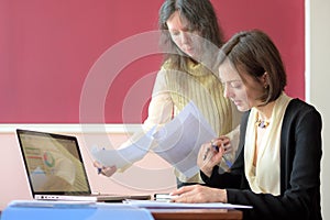 Young smartly dressed lady helps another young lady to work with documents, fill forms and sign