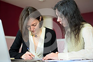 Young smartly dressed lady helps another young lady to work with documents, fill forms and sign photo