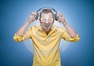 Young smile man with earphones enjoying while listen music over blue background, dresses in yellow shirt. Joyful man with