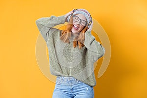 Young smile woman with earphones enjoying while listen music, isolated on yellow background. Joyful woman with headphones.