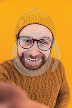 Young smiley man in selfie camera - Caucasian bearded hipster holding a smartphone and talking using videocall - orange