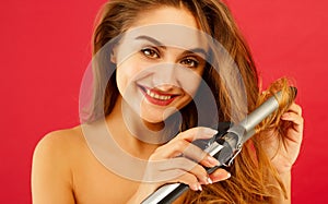 Young smiley woman making curly hair by ploy over red background