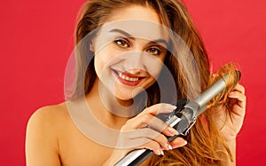 Young smiley woman making curly hair by ploy over red background photo
