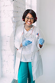 Young smiling African American doctor in medical mask holding a syringe