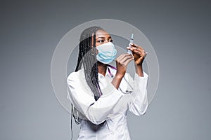 Young smiling African American doctor in medical mask holding a syringe isolated on gray