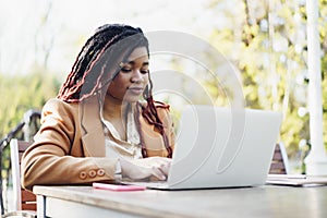 Young smiling african american woman sitting at the table in street cafe and using laptop