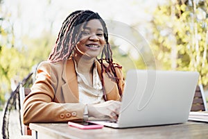 Young smiling african american woman sitting at the table in street cafe and using laptop