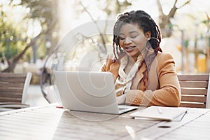 Young smiling african american woman sitting at the table in street cafe and using laptop