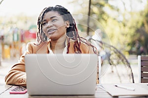 Young smiling african american woman sitting at the table in street cafe and using laptop