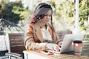 Young smiling african american woman sitting at the table in street cafe and using laptop