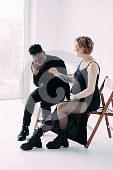 Young smiling african man and his caucasian pregnant woman sit on chairs