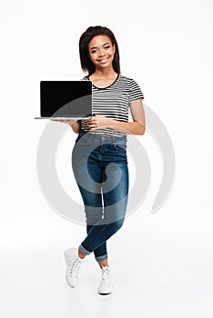 Young smiling african woman standing and holding blank screen laptop