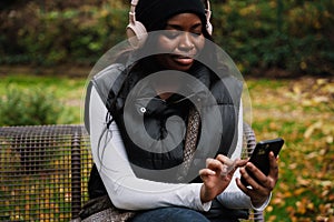 Young smiling afro woman using mobile phone while sitting in park