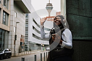 Young smiling afro woman using mobile phone and waving while standing outdoors