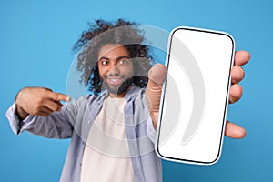 Young smiling Arabian man with phone in hand points finger at white display