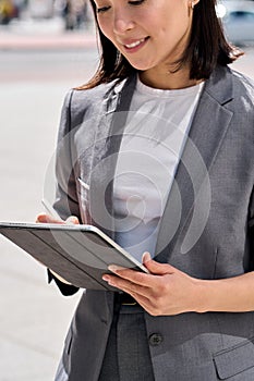 Young smiling Asian entrepreneur standing on city street using digital tablet.