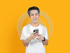 Young smiling Asian man with holding smart phone on orange background. copy space for put advertisement.
