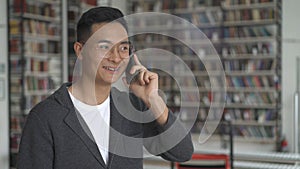 Young smiling asian man talking on the phone, teeth braces, in library