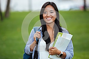 Young smiling asian student woman with backpack, holding notebook, outdoor