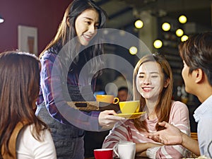 Young smiling asian waitress serving coffee to customers