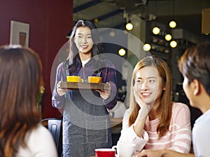 Young smiling asian waitress serving coffee to customers photo