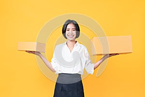 Young smiling asian woman hands showing cardboard boxes on light orange background.