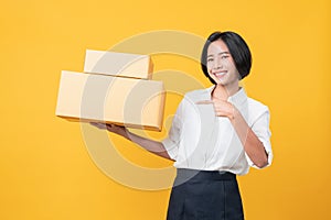 Young smiling asian woman hands showing cardboard boxes and pointing on light orange background.