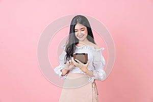 Young smiling Asian woman holding digital tablet and looking to screen on pink background.