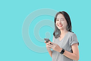 Young smiling Asian woman holding smartphone and wear smartwatch isolated on light blue background.