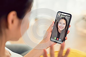 Young smiling Asian woman making video call online talking with friends to smartphone from home.