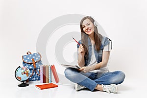 Young smiling attractive woman student in headphones listen music holding notebook, pencil near globe, backpack, school