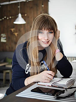 Young smiling attractive young woman with pen in hand thinking on plans and writing list to do in notepad enjoying