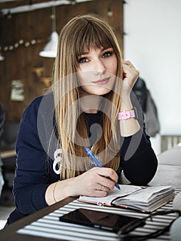 Young smiling attractive young woman with pen in hand thinking on plans and writing list to do in notepad enjoying