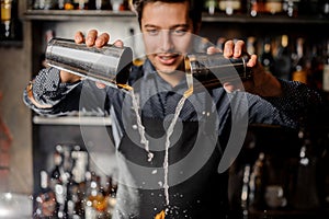 Young smiling barman pouring drink with slices of fresh orange fruit