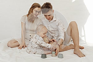 Young smiling beauteous family with cherubic infant baby playing with modern pastel silicone bowls of different size. photo