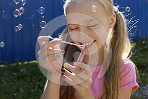 A young smiling beautiful blonde girl inflates soap bubbles in the summer