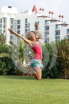 Young smiling beautiful curly blonde hair slim girl fashion portrait in pink T-shirt jumping in the field summer time green grass