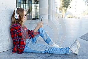 Young smiling beautiful hipster happy teen girl in city street,speaking on smartphone,headphones, jeans, backpack