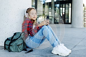 Young smiling beautiful hipster happy teen girl in city street,speaking on smartphone,headphones, jeans, backpack