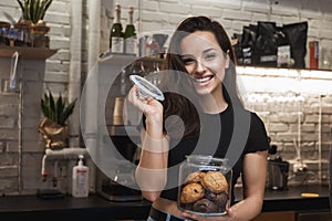 Young smiling beautiful woman barista enjoying nice aroma while opening jar with cookies lokking happy