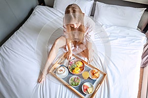 Young Smiling Beautiful Woman Having Breakfast in Bed in Cozy Hotel Room